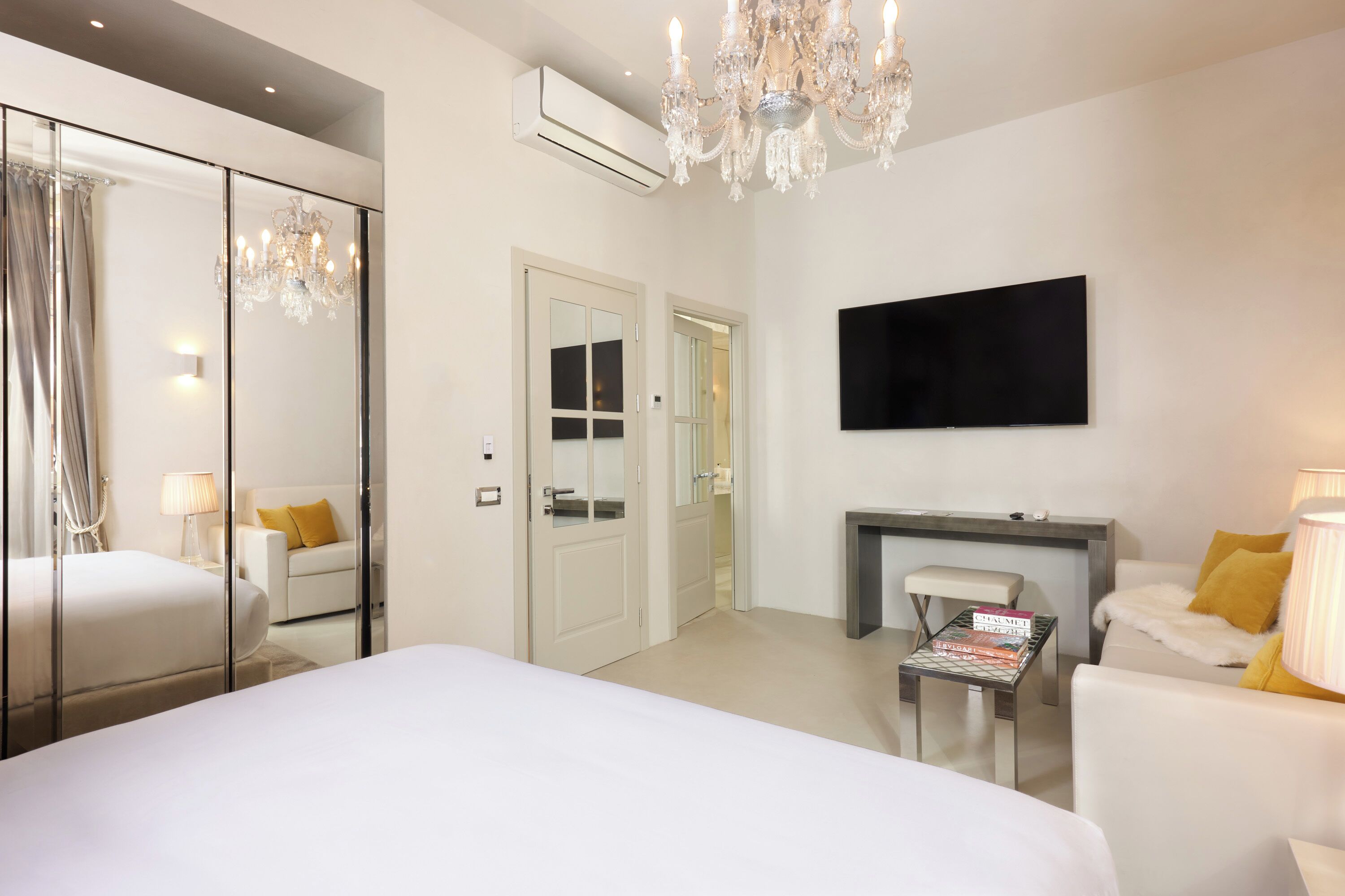 Habitación de hotel con una cama grande, un candelabro, un televisor de pantalla plana y un rincón de descanso con mesa y sillas.
