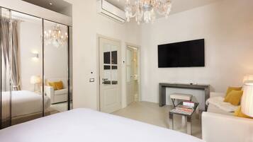 Habitación de hotel con una cama grande, un candelabro, un televisor de pantalla plana y un rincón de descanso con mesa y sillas.