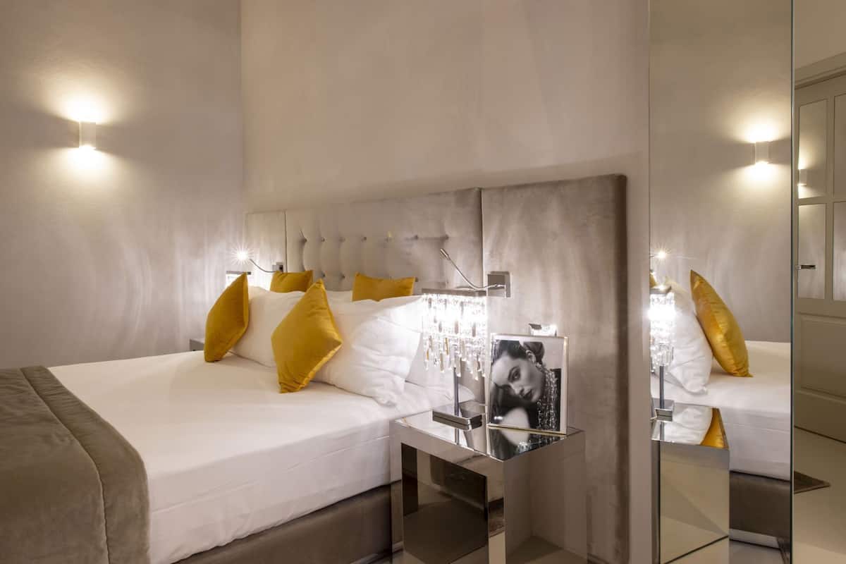Une chambre d’hôtel moderne avec un grand lit, une table de chevet avec un miroir et un luminaire fixé au mur.