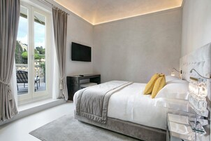 A modern bedroom with a large bed, a flat-screen TV, a bedside table, and a view of the outdoors.