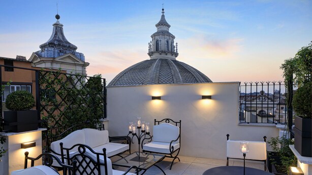 Una terraza en la azotea con mobiliario exterior, una estructura en forma de cúpula al fondo y vistas de la ciudad.