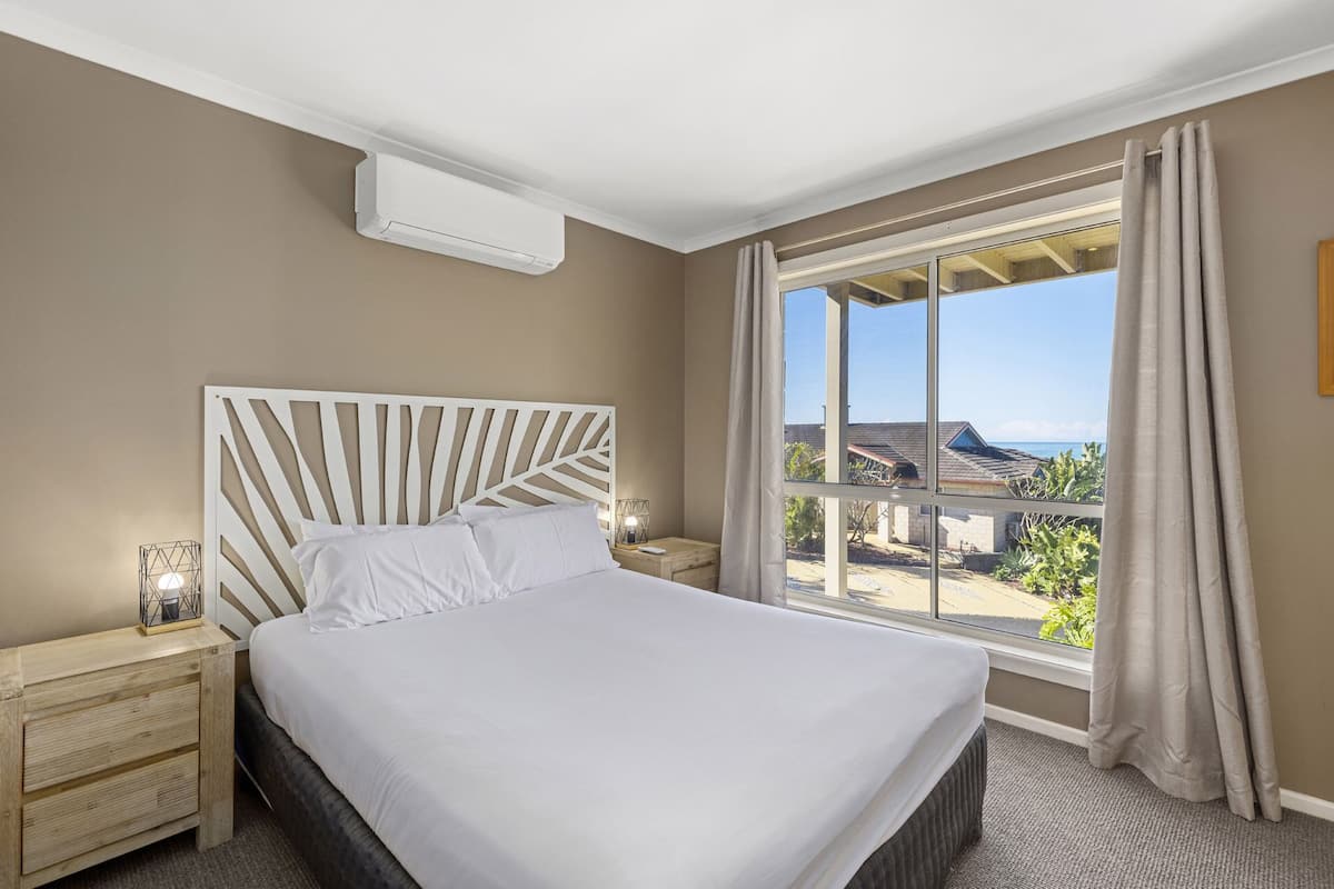A hotel room with a large bed, a nightstand, a bedside lamp, and a window with curtains.