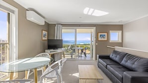 A living room with a TV, a glass table, a sofa, and a view of the ocean. - Aqualuna Beach Resort (Korora)