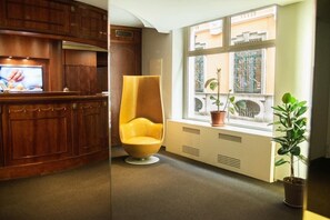 A modern room with wooden cabinets, a yellow chair, a window with plants, and a TV on the left. - Hotel Alli Due Buoi Rossi (Alessandria)