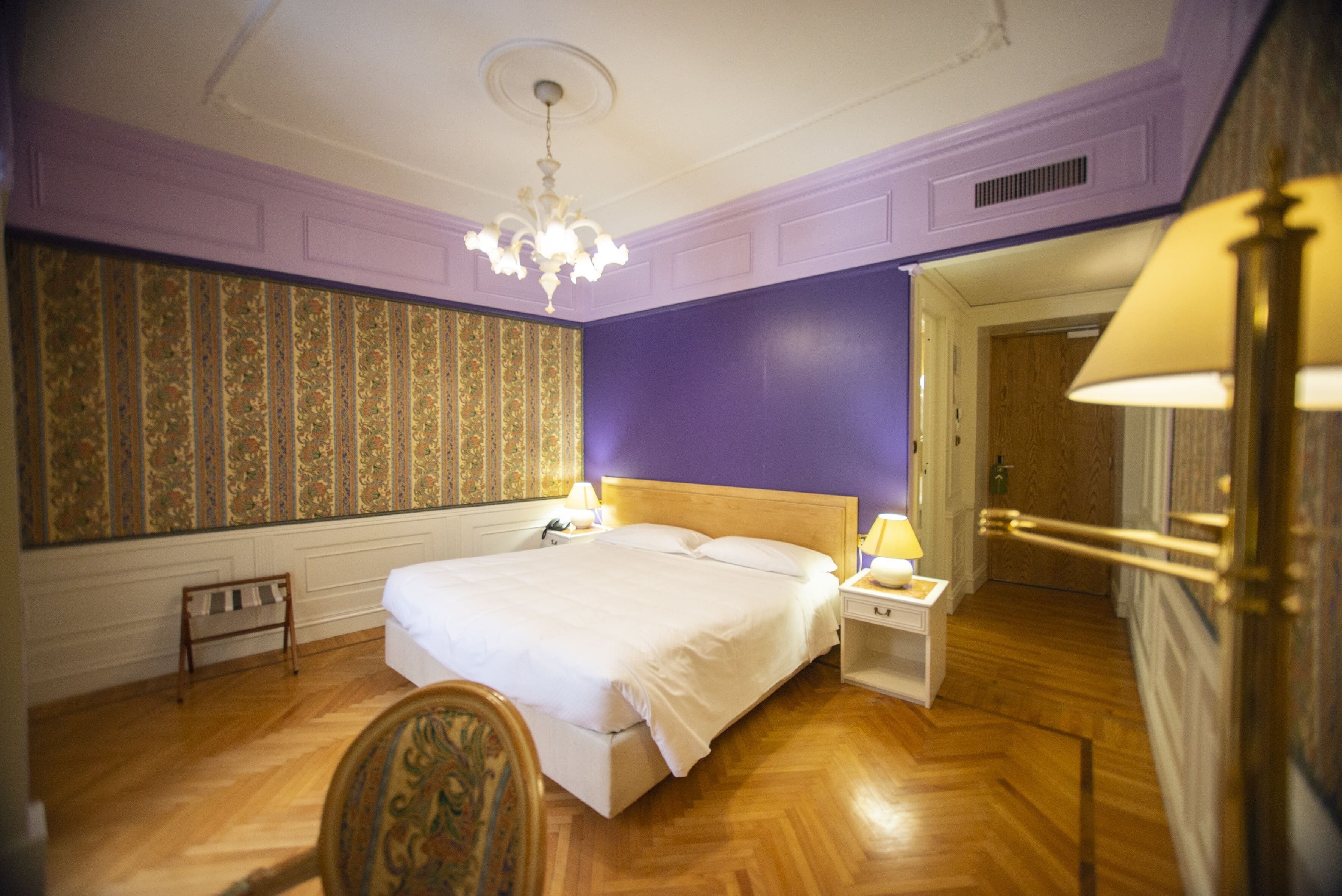 Ein Schlafzimmer mit einem großen Bett, einem Nachttisch, einem Sessel und einer Tür zu einem anderen Raum.