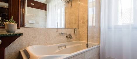 A modern bathroom with a large bathtub, a glass shower enclosure, and a marble-tiled wall.