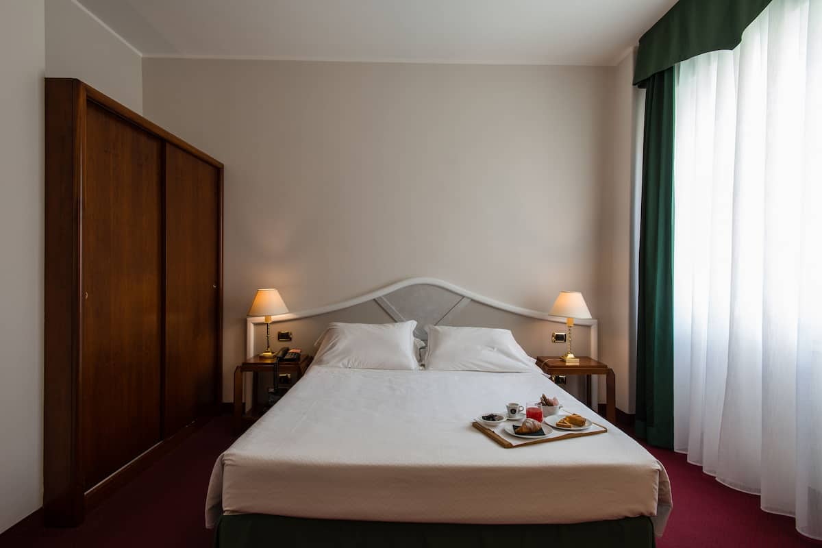 Een hotelkamer met een bed, twee nachtkastjes met lampen, een kledingkast en een ontbijttray op het bed.