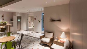 Een moderne hotellobby met een eetgedeelte, een zithoek met een lamp en een decoratief wandobject.