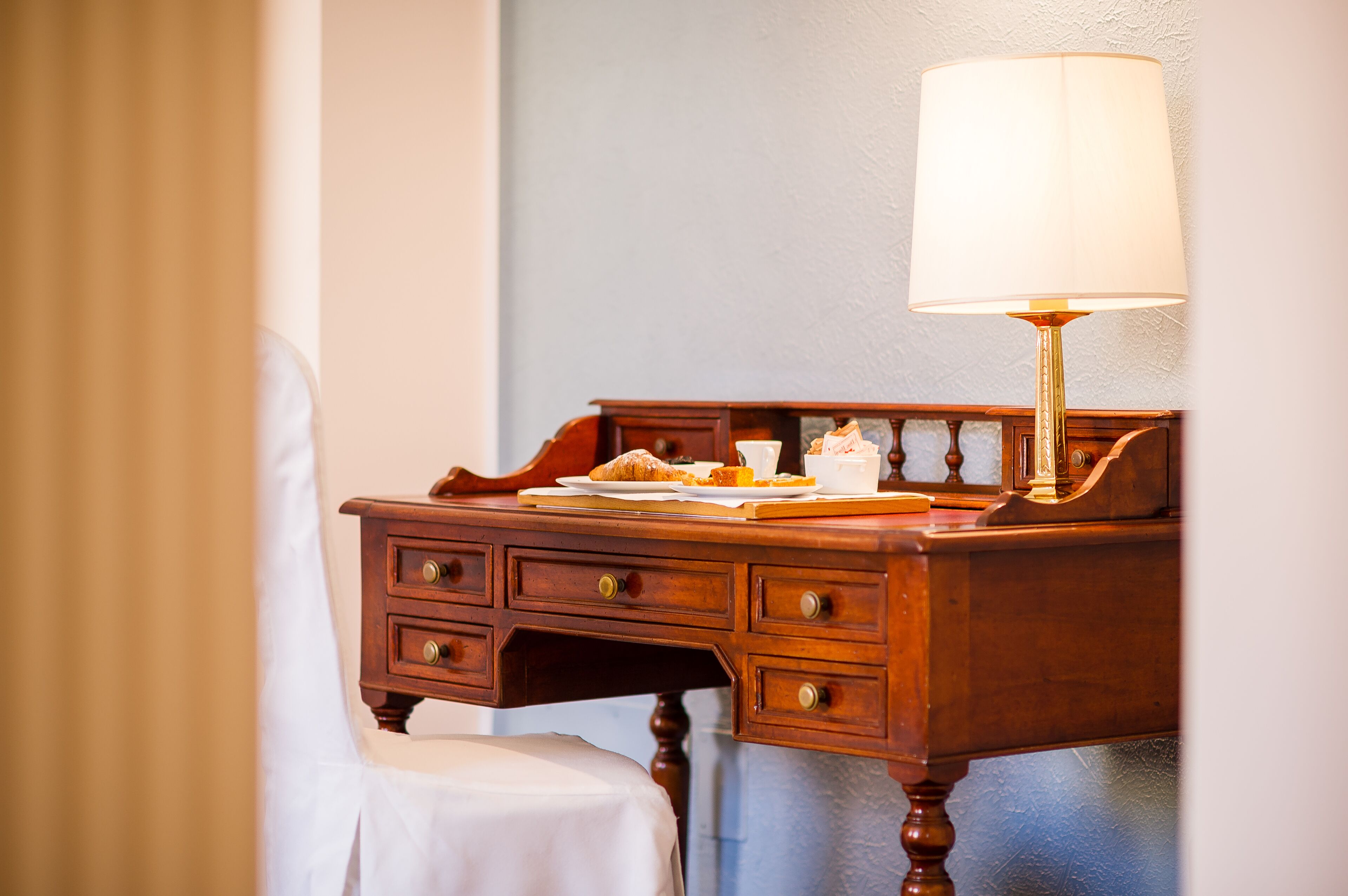 A wooden desk with a lamp, a plate of food, and a cup.
