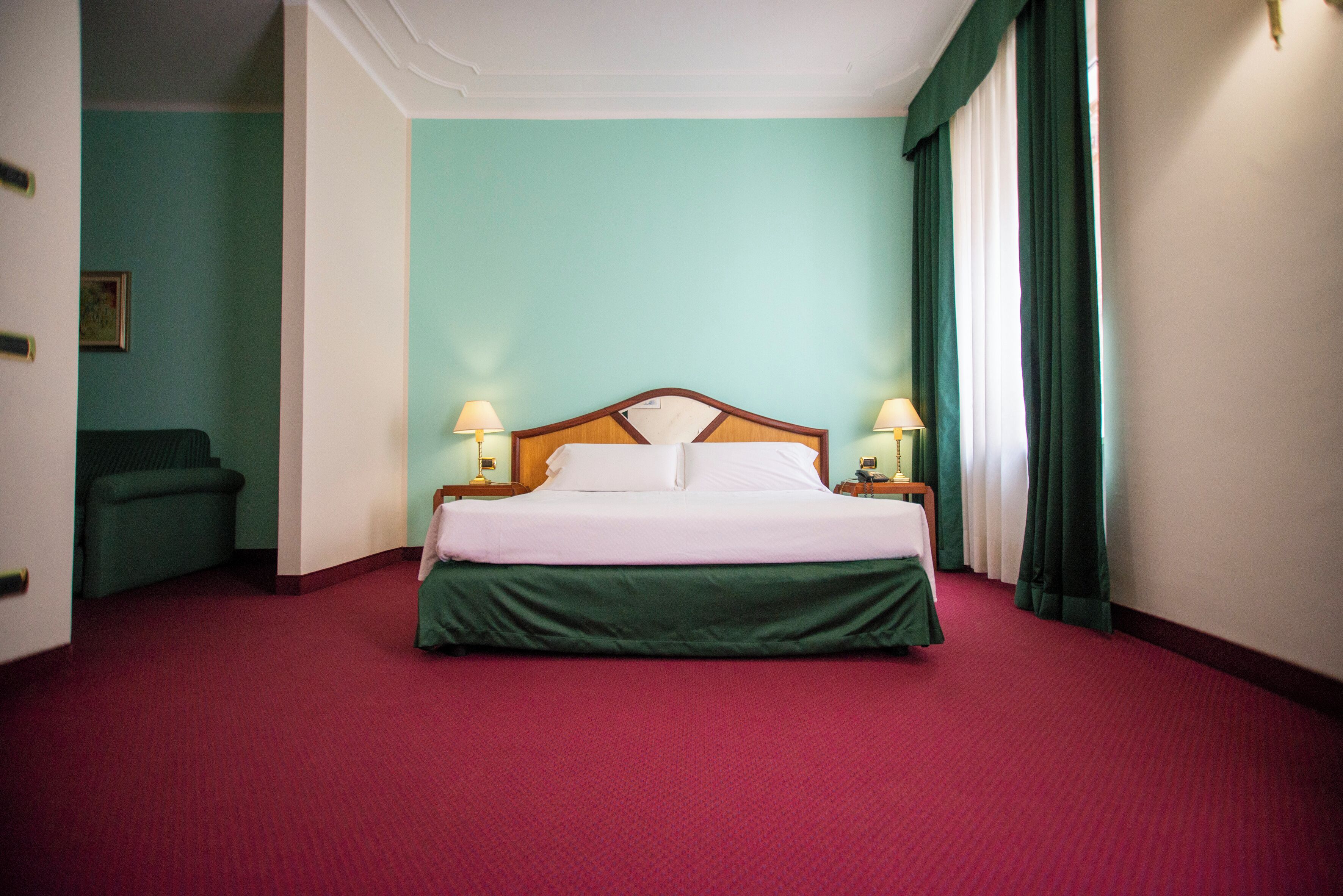 Ein Hotelzimmer mit einem großen Bett, grünen Vorhängen und zwei Nachttischlampen.