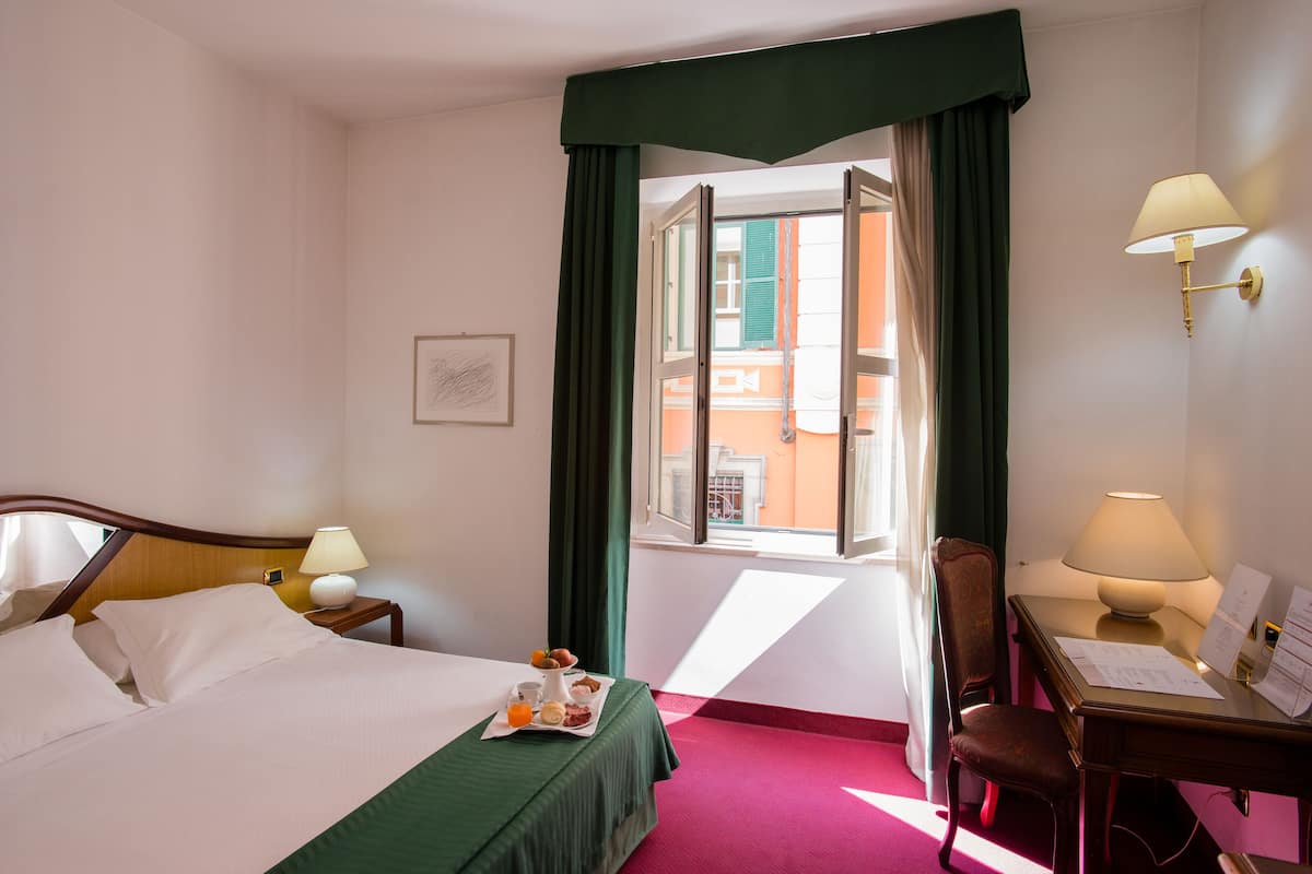 Een hotelkamer met een bed, een bureau met lamp, een stoel en een raam met gordijnen.