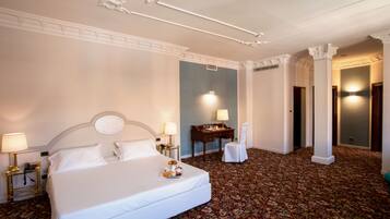 Habitación de hotel con una cama grande, dos mesitas de noche con lámparas, un escritorio con silla y un pilar decorativo.