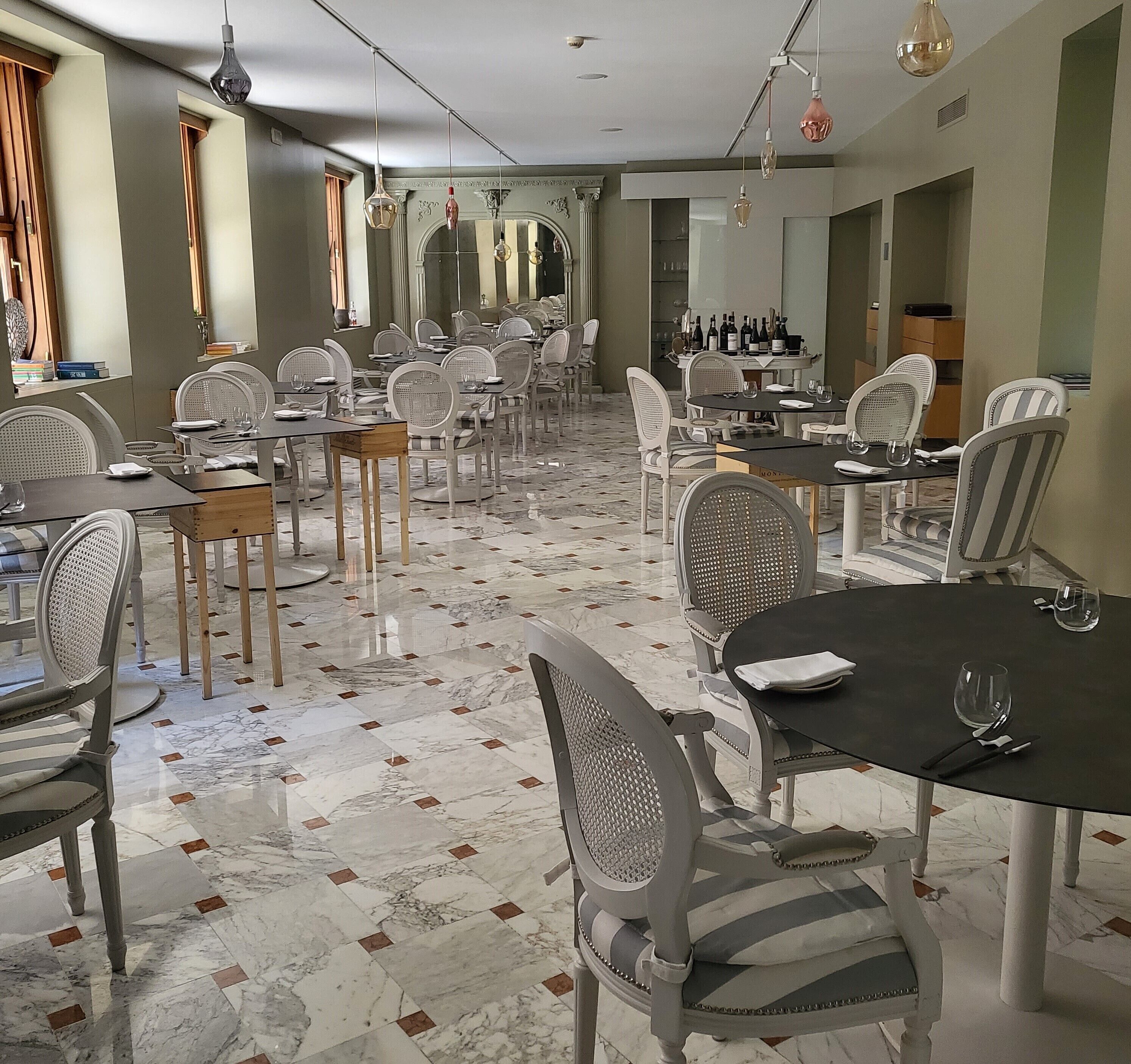 A spacious dining area with marble flooring, white upholstered chairs, and hanging pendant lights.