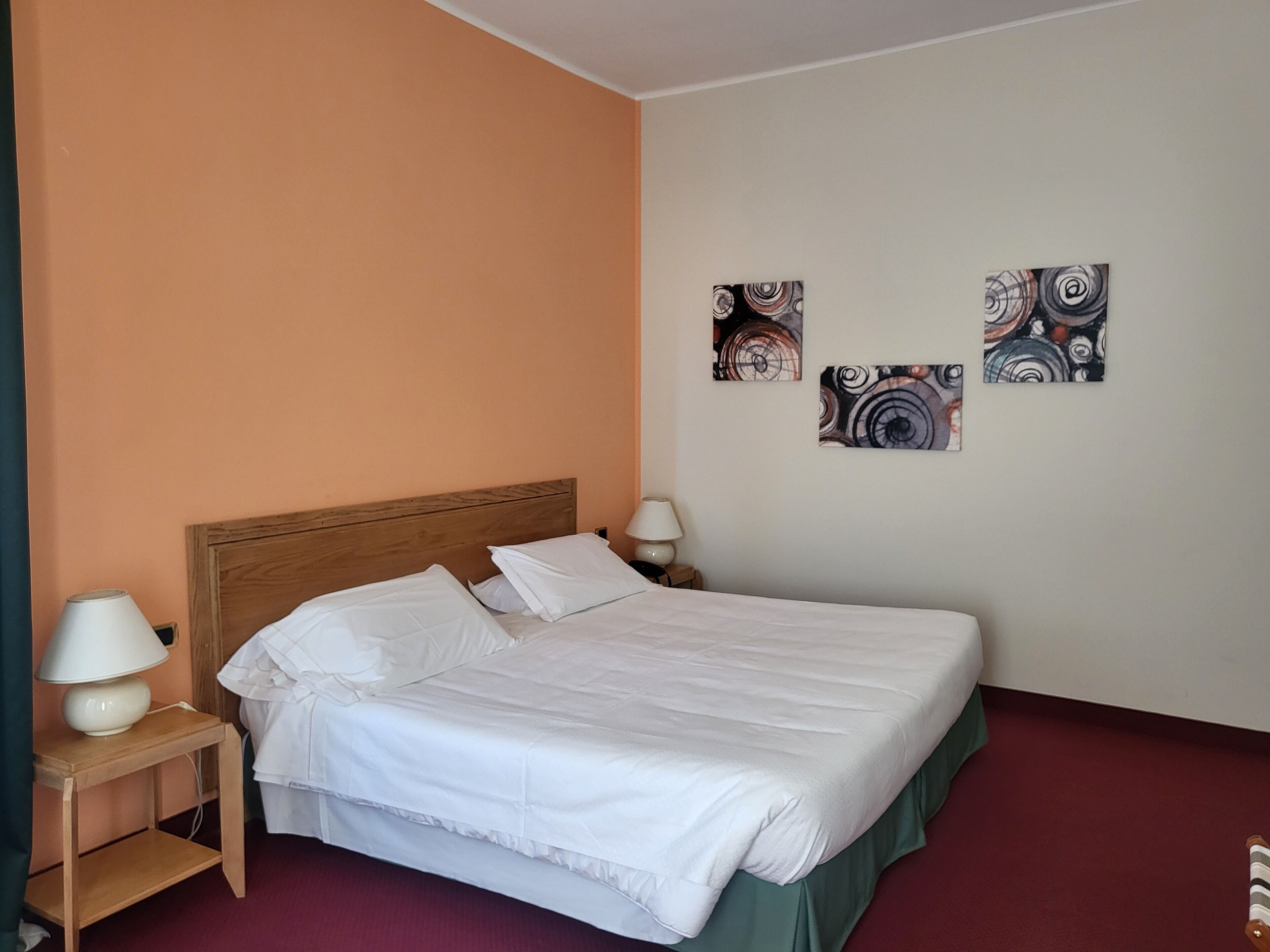 A neatly made bed with white linens, a wooden headboard, and a green skirt. There are two bedside tables with lamps, and abstract art on the wall.