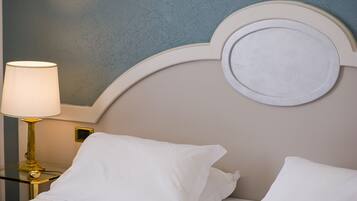 Una cama bien hecha con sábanas y almohadas blancas, una lámpara de noche, y una pared con textura azul y un adorno circular.