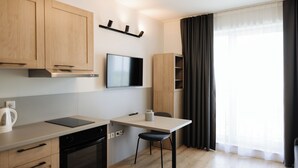 A modern kitchen with wooden cabinets, a built-in oven, a dishwasher, and a flat-screen TV mounted on the wall.