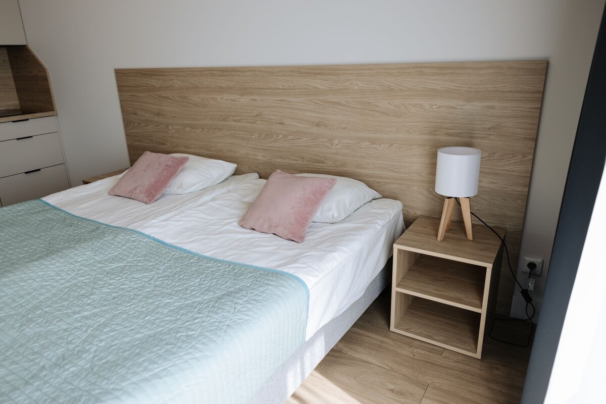 A neatly made bed with a wooden headboard, two pillows, and a bedside table with a lamp.