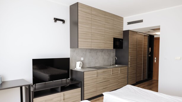A modern hotel room with a kitchenette, a TV, a bed, and a desk.