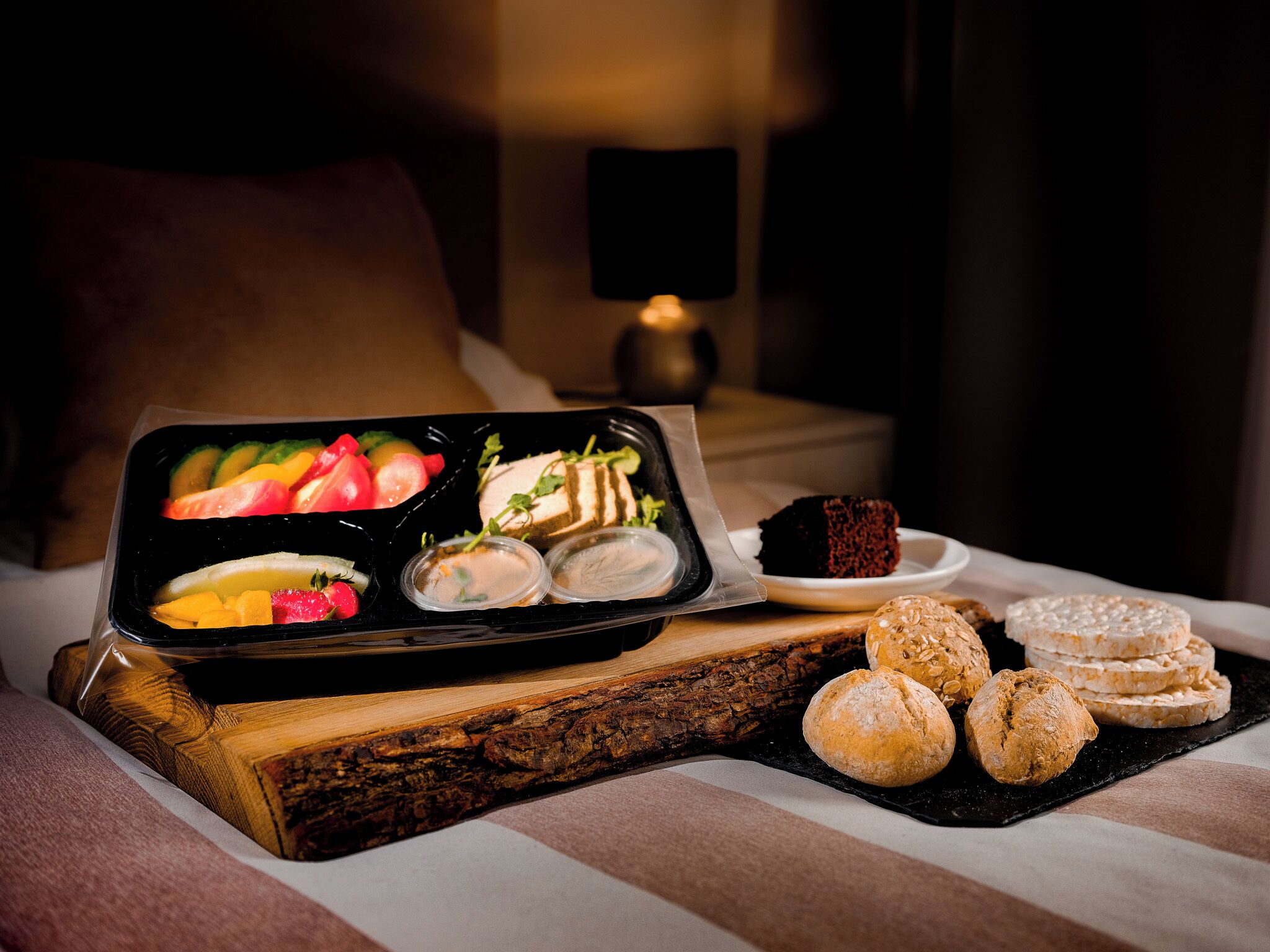Una bandeja con frutas, pasteles y un postre sobre una mesa de madera en una habitación con poca luz.