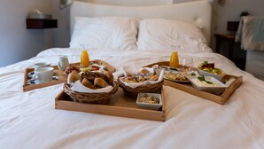 Ein ordentlich gemachtes Bett mit Frühstückswagen, auf denen Brot, Gebäck, Obst und Getränke bereitstehen.