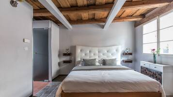 A bedroom with a wooden ceiling, a large bed with a tufted headboard, bedside tables with decorative items, and a window with a view.