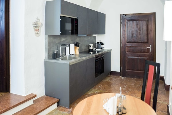 Una cocina compacta con armarios grises, microondas integrado, cafetera y una mesa de comedor de madera con una silla.