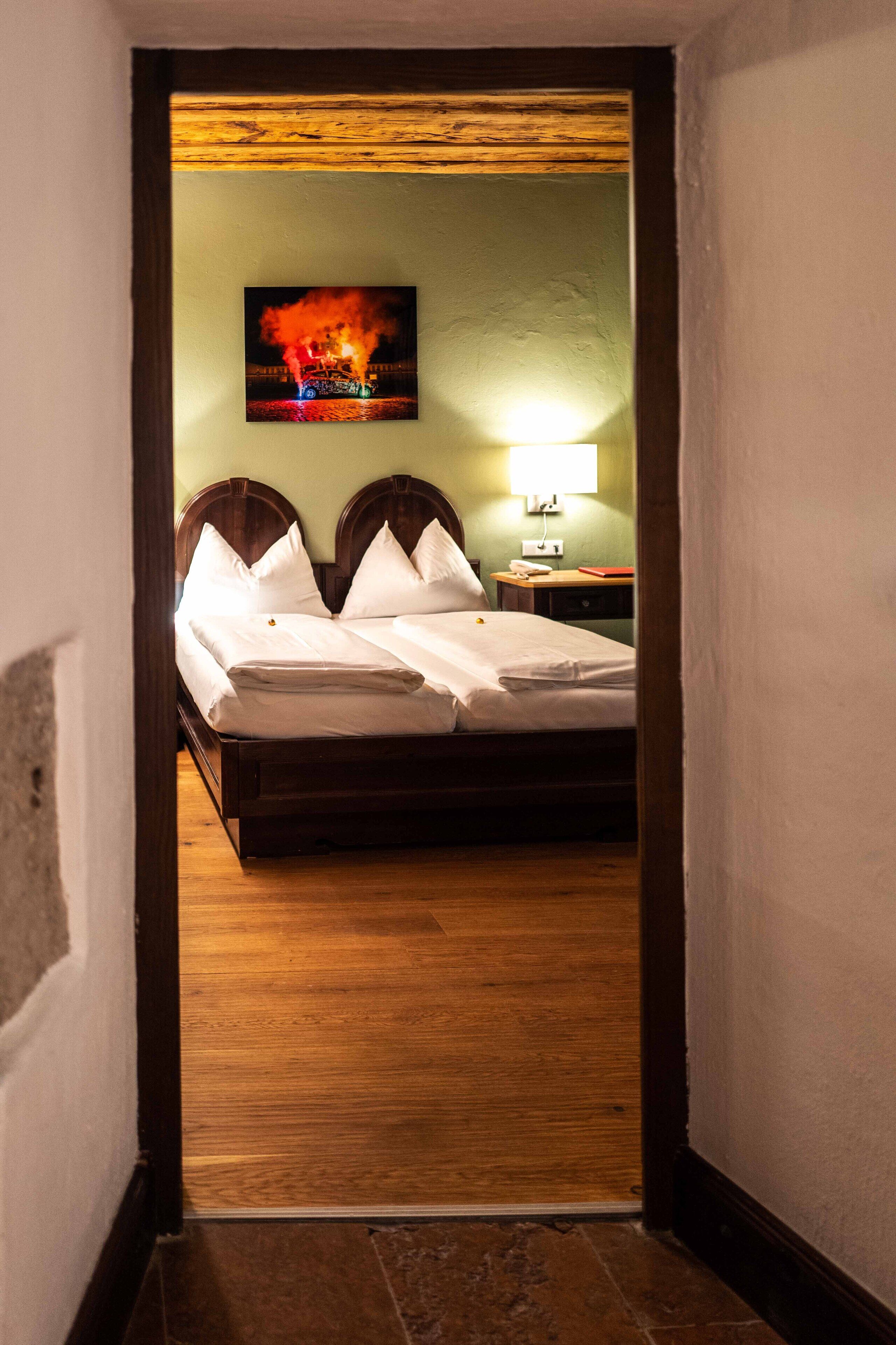A hotel room with a wooden bed, a nightstand, a lamp, and a painting on the wall.
