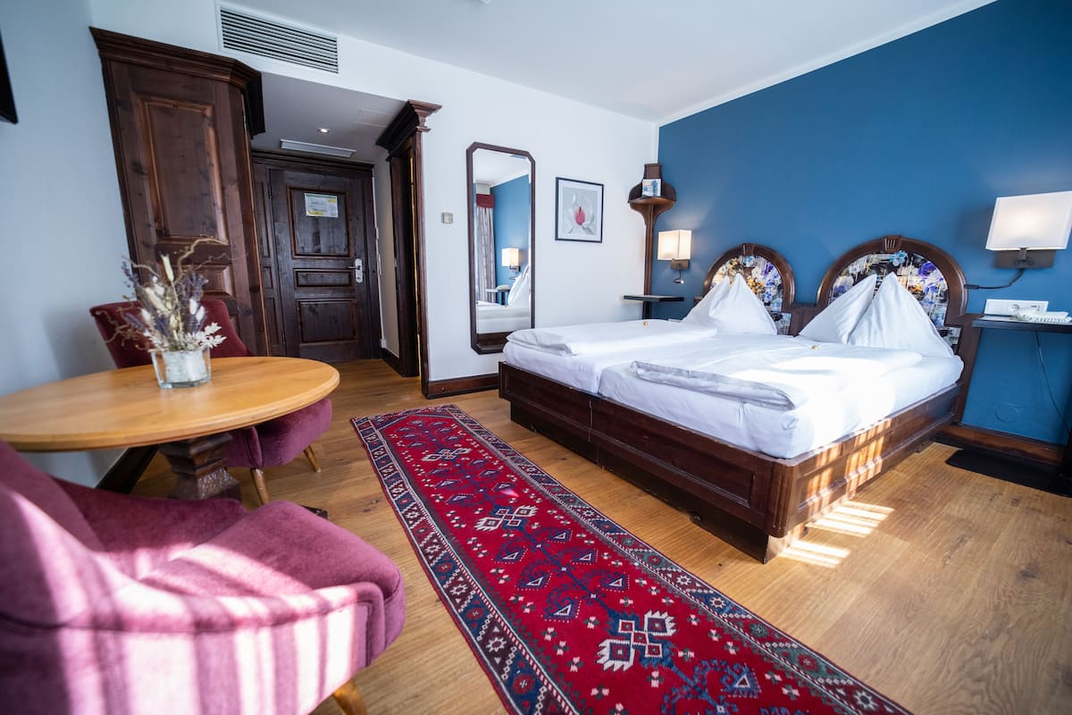 A hotel room with a large bed, a desk, a chair, and a red carpet.