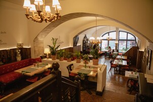 Un restaurante con techos altos abovedados, mesas de madera con manteles individuales verdes, bancos acolchados rojos y plantas en macetas.