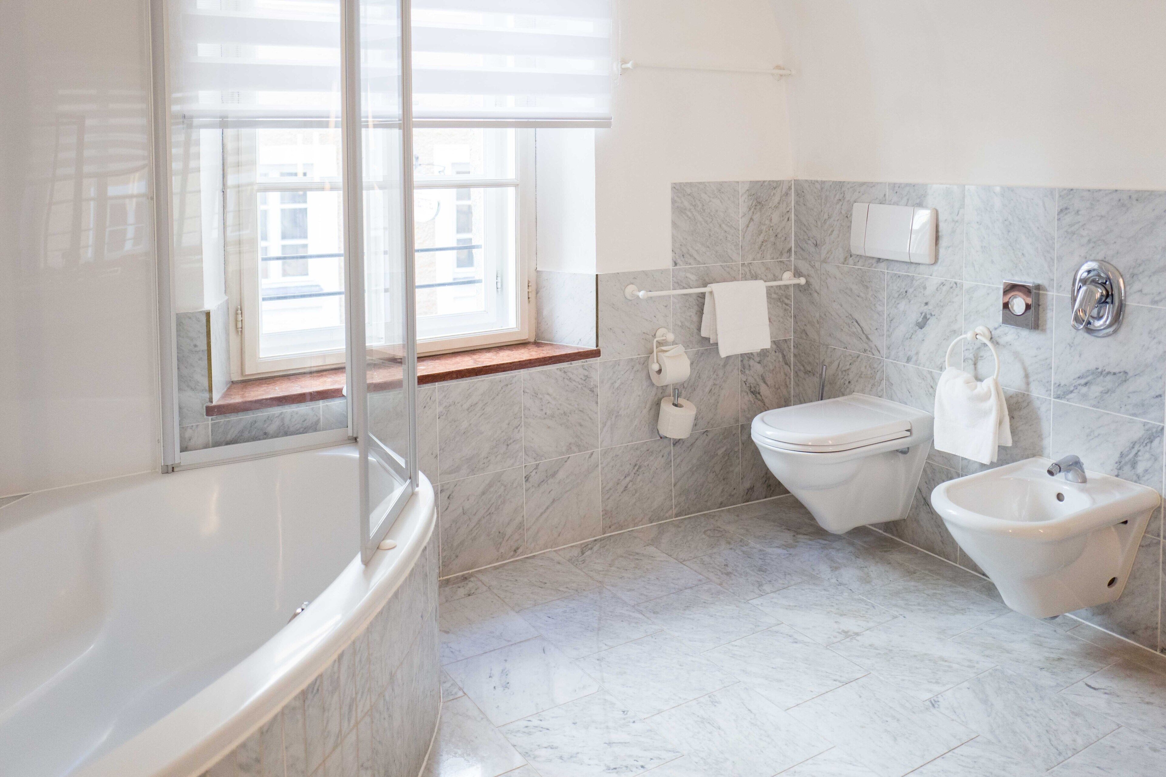Un baño moderno con bañera, inodoro, bidé y ventana que proporciona luz natural.