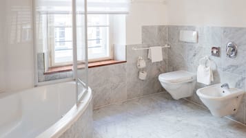 Un baño moderno con bañera, inodoro, bidé y ventana que proporciona luz natural.