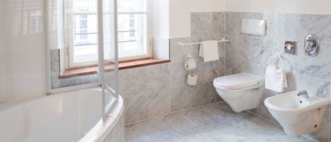 Un baño moderno con bañera, inodoro, bidé y ventana que proporciona luz natural.