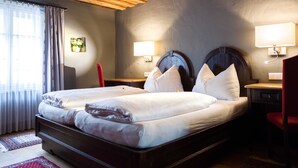 A double bed with two pillows, a wooden headboard, bedside lamps, and a red chair. - Altstadthotel Stadtkrug (Salzburg)