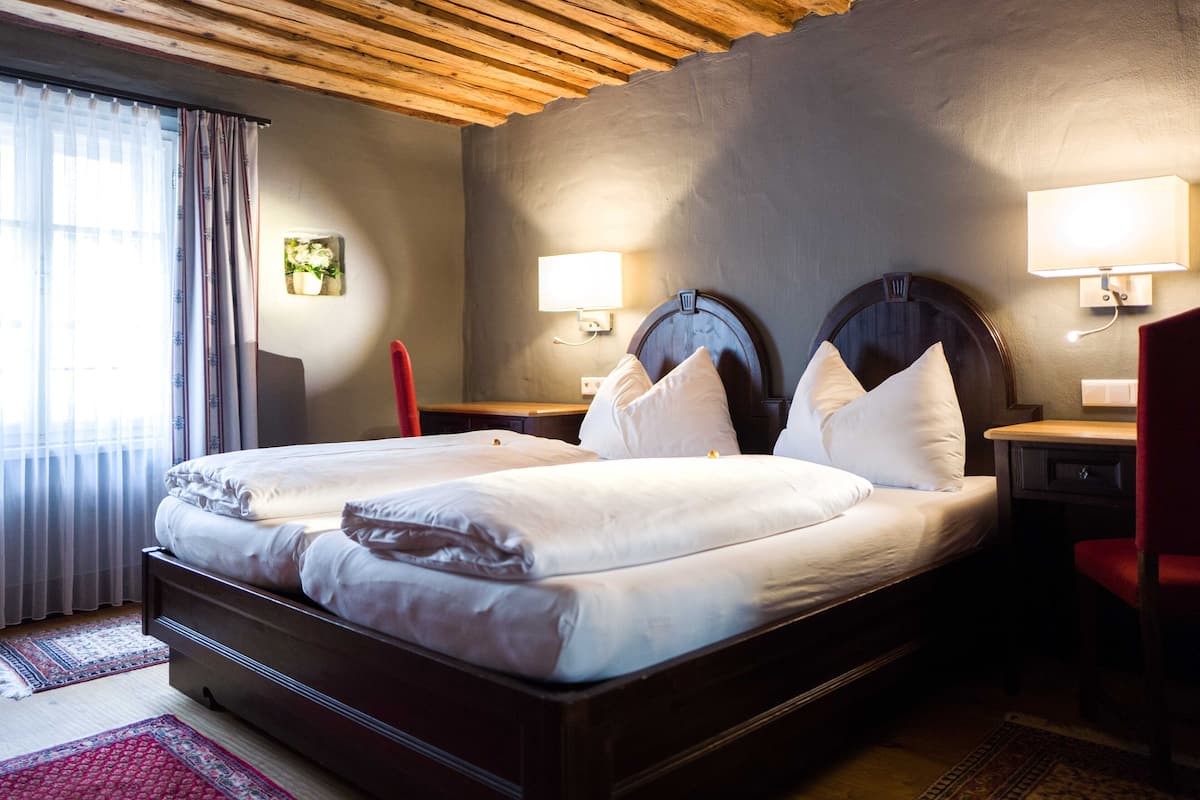 A double bed with two pillows, a wooden headboard, bedside lamps, and a red chair.