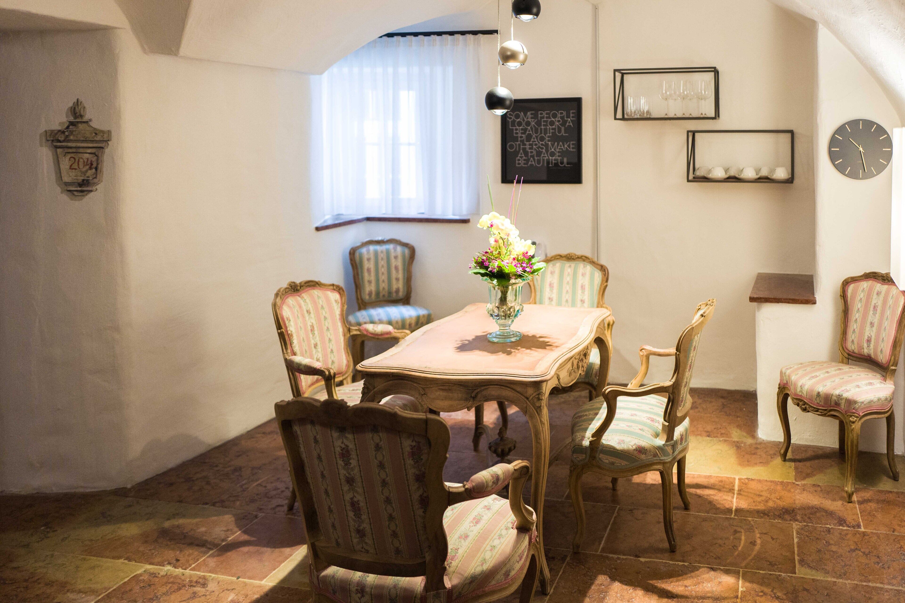 A dining area with a table and chairs, a vase with flowers, and a clock on the wall.