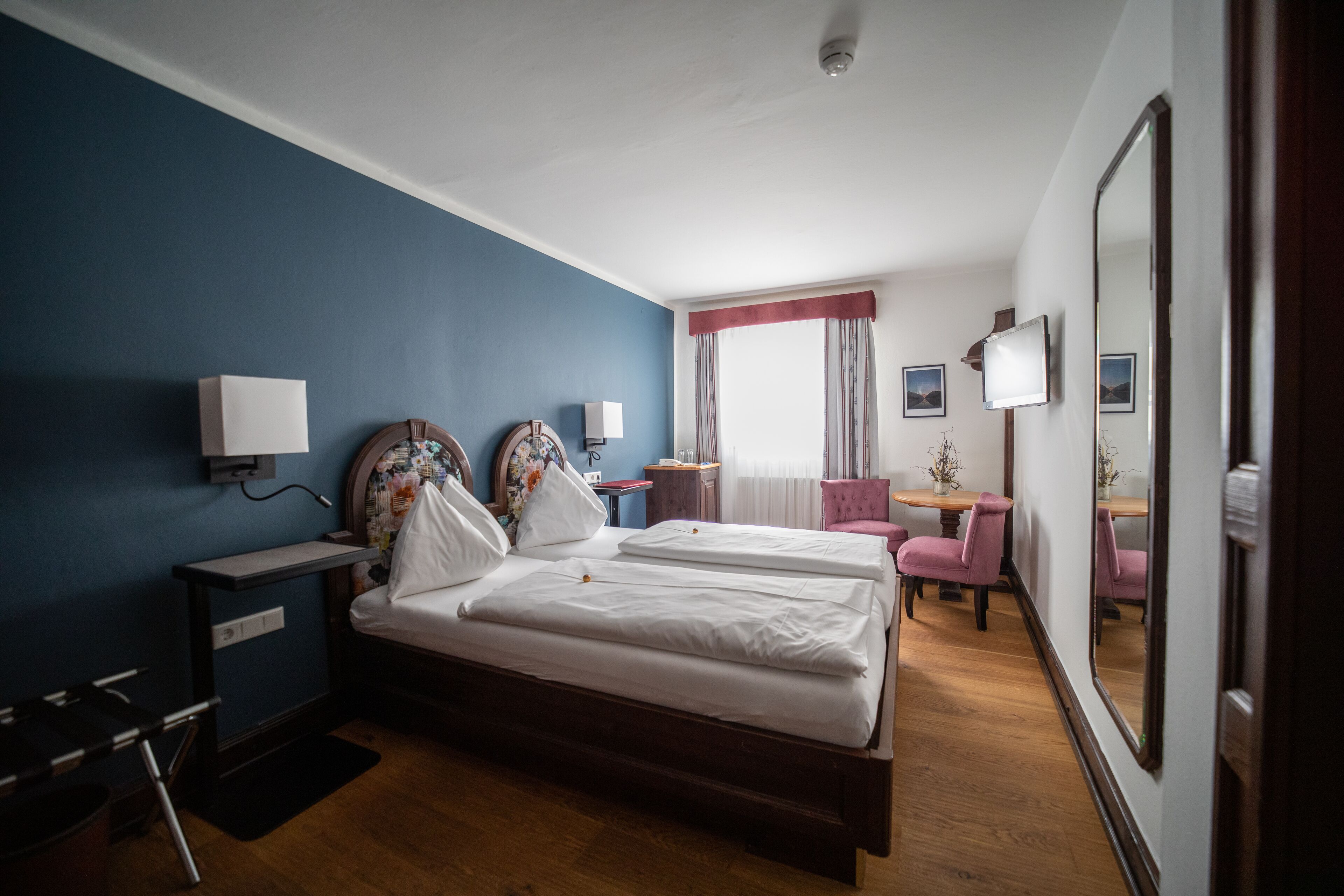 A hotel room with a double bed, bedside tables, a desk, a chair, and a large mirror.