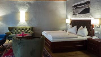 Ein Hotelzimmer mit einem Bett, einem grünen Sessel, einem Nachttisch aus Holz und einem an der Wand hängenden Bild.