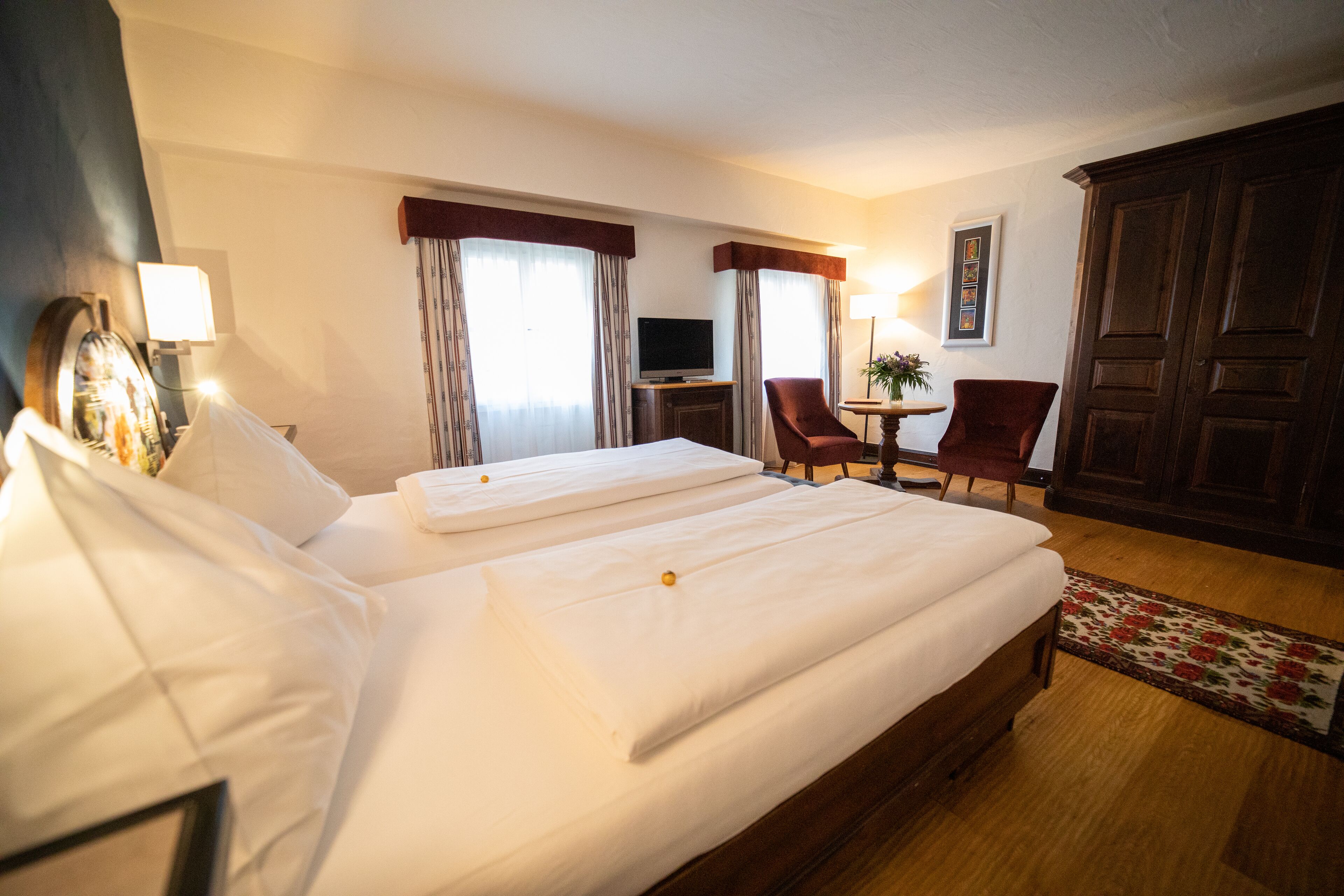 A hotel room with two beds, a TV, a desk with a chair, and a large wooden wardrobe.