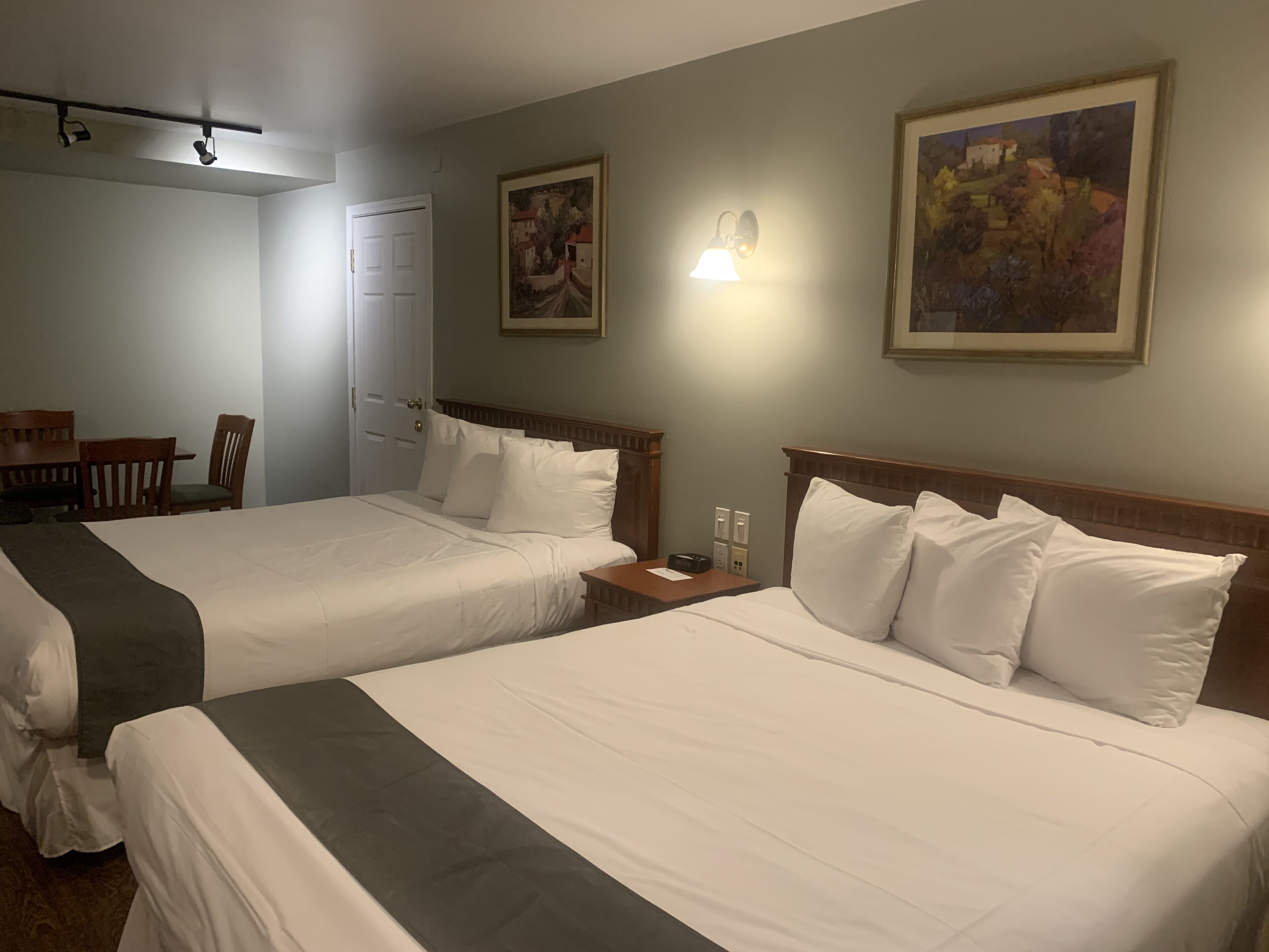 Habitación de hotel con dos camas, un escritorio, una silla y dos cuadros en las paredes.