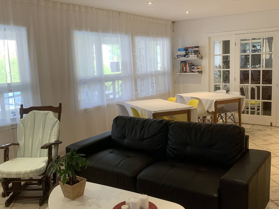 Una sala de estar con un sofá negro, una silla de madera, una mesa blanca con una bandeja roja y una planta en maceta.