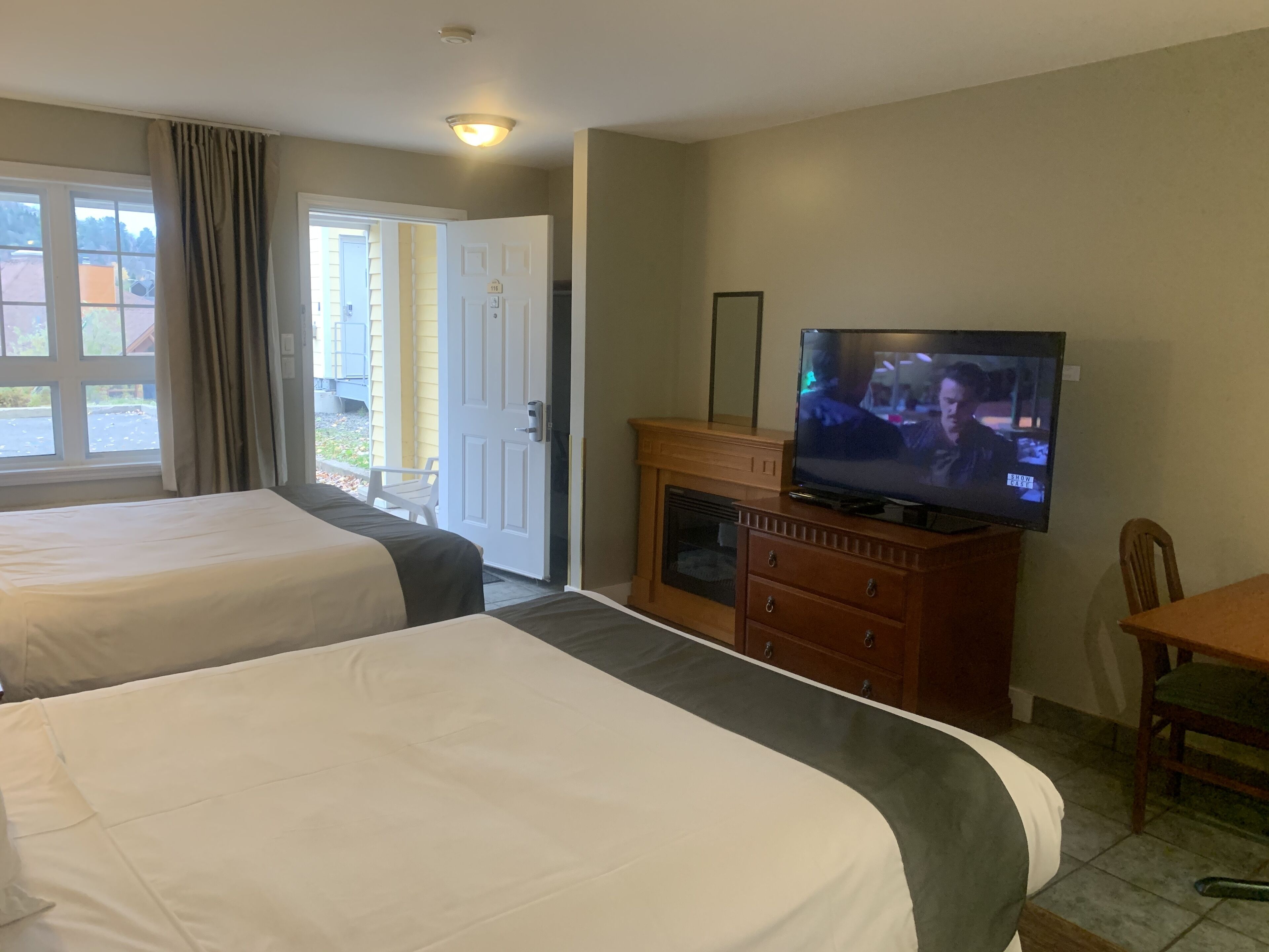 Ein Hotelzimmer mit zwei Betten, einem Fernseher, einer Holzkommode und einer Tür, die nach draußen führt.