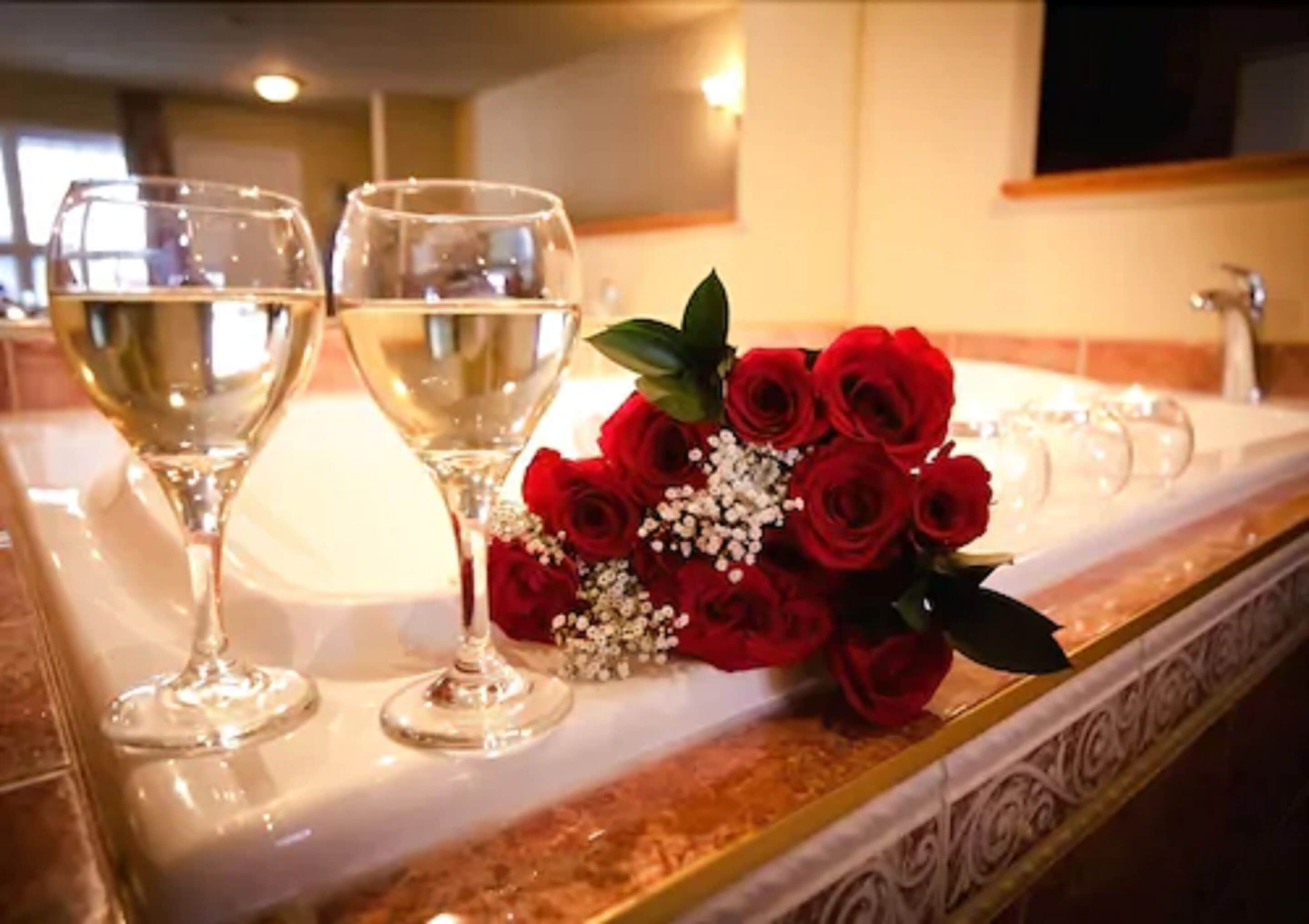 A countertop with two glasses of white wine, a bouquet of red roses, and a decorative tray.