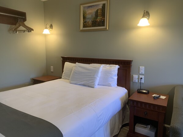 A neatly made bed with white linens, a wooden headboard, and two bedside lamps.