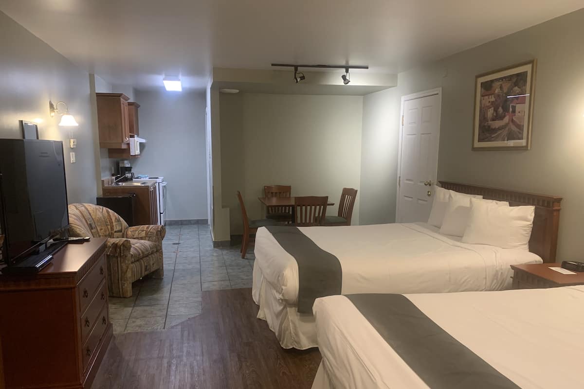 A hotel room with two beds, a desk with a computer, a chair, a small table, and a painting on the wall.