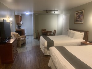 A hotel room with two beds, a desk with a computer, a chair, a small table, and a painting on the wall. - Hotel & Suites Les Laurentides Saint Sauveur (Saint-Sauveur)