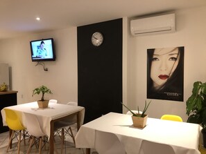 A dining area with a white table, yellow chairs, a clock, and a poster on the wall. - Hotel & Suites Les Laurentides Saint Sauveur (Saint-Sauveur)