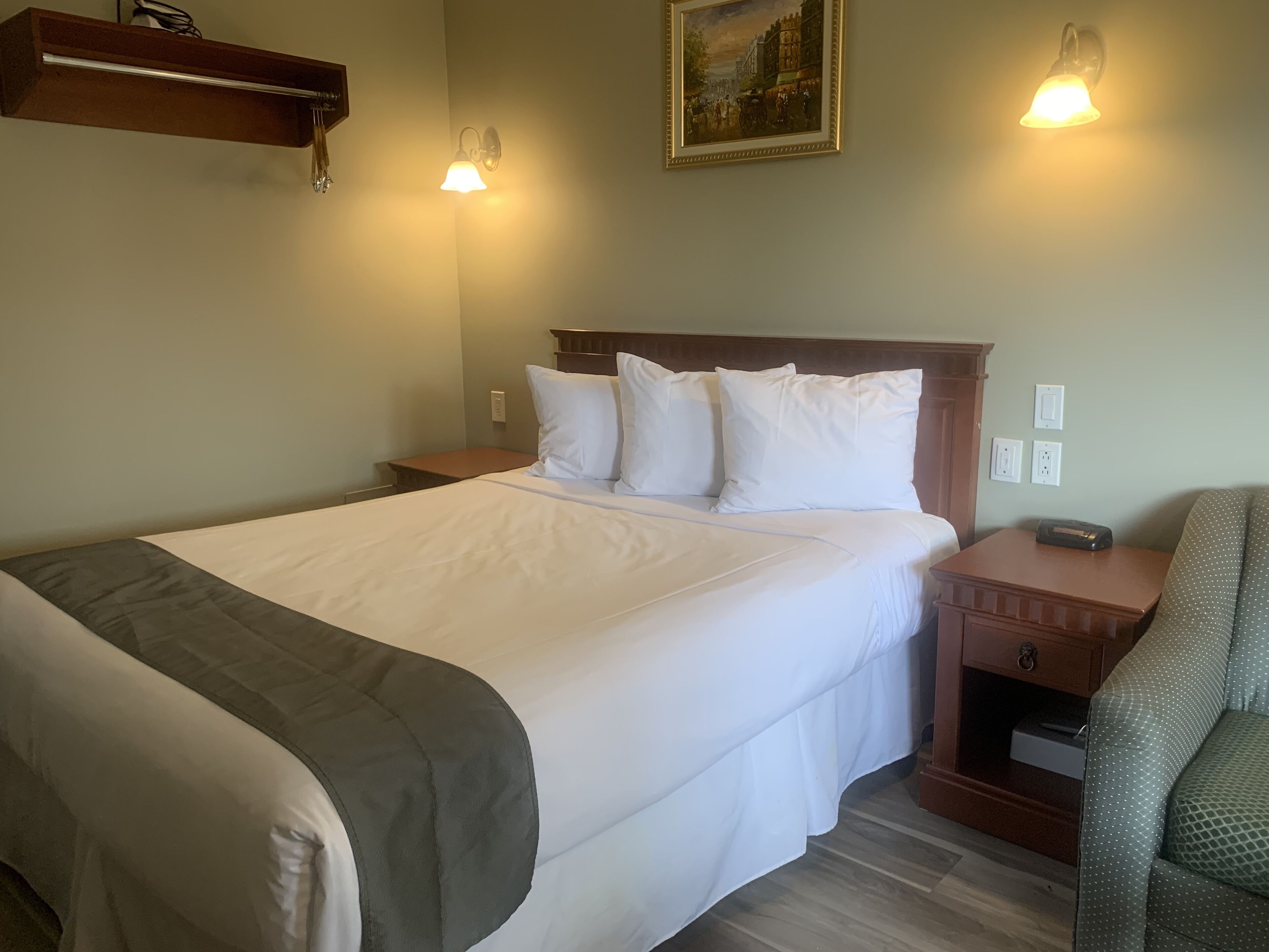 Quarto de hotel com uma cama grande, duas mesas de cabeceira, um criado-mudo, uma cadeira e um quadro na parede.
