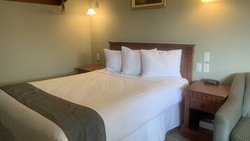 Quarto de hotel com uma cama grande, duas mesas de cabeceira, um criado-mudo, uma cadeira e um quadro na parede.