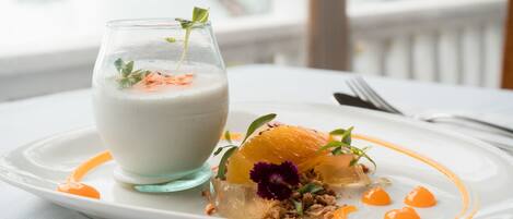A dessert plate with a glass of a creamy beverage, garnished with orange slices and edible flowers.