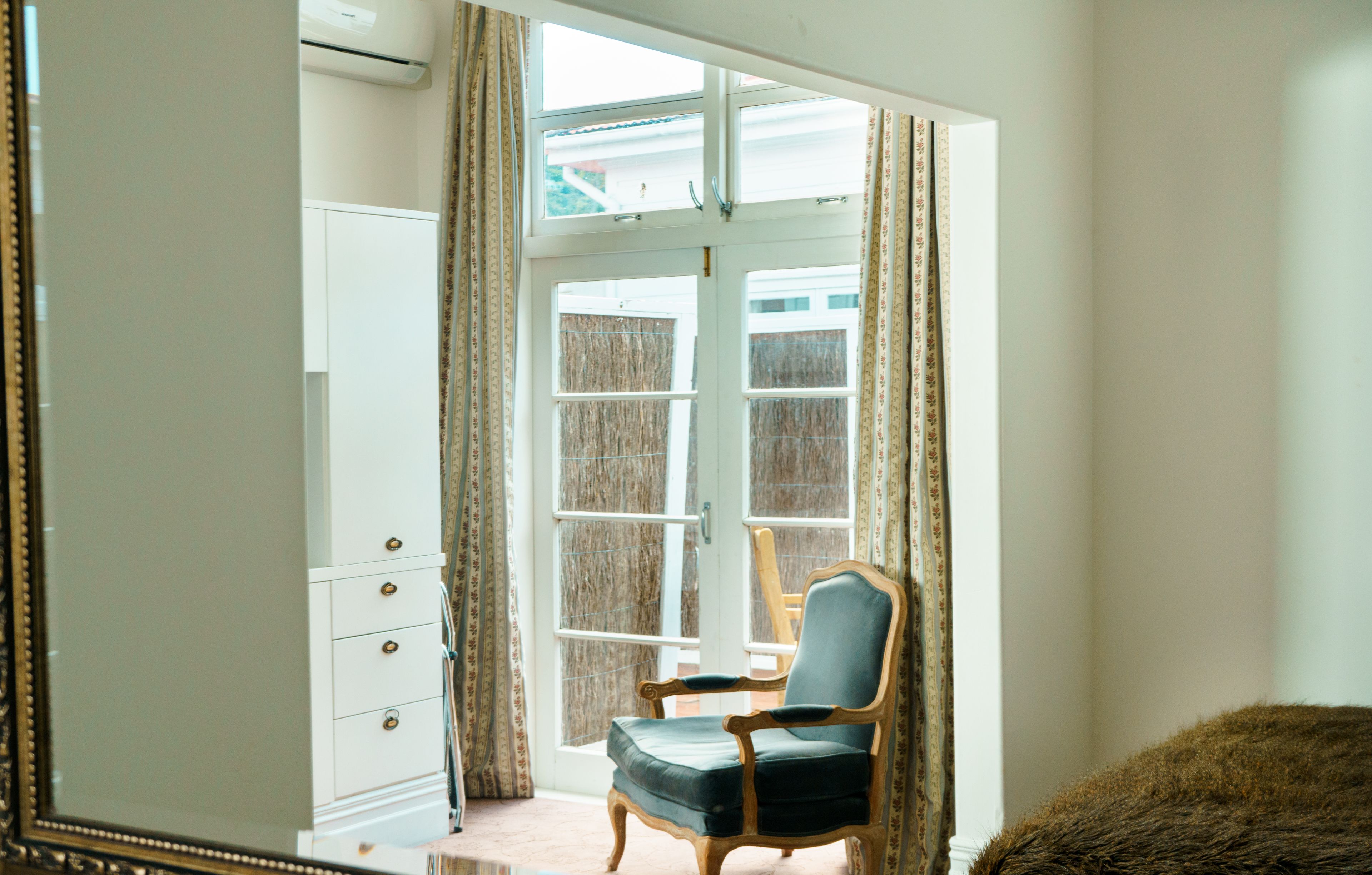 A room with a large window, a chair, a wardrobe, and a mirror.